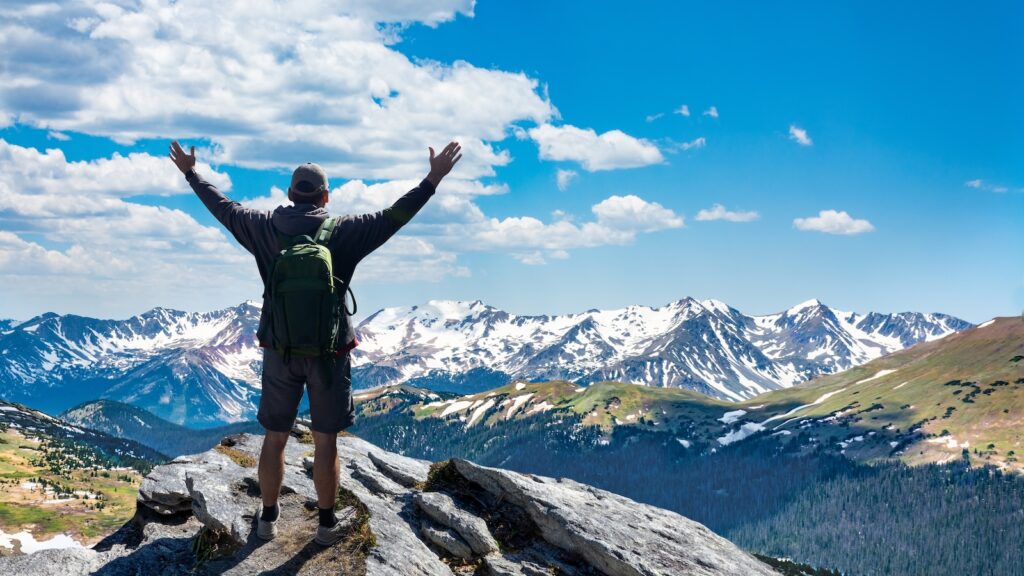 Hiker with arms up standing on the top of the mountain - Successful man enjoying triumph - Sport and success concept. Rocky Mountains National Park, Colorado, USA.