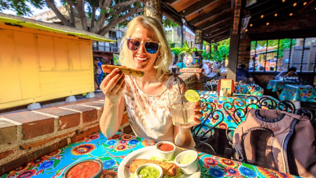 El Pueblo de Los Angeles State Historic Landmark, California, United States. Happy tourist woman drinks Margarita, Mexican cocktail, and eats enchilada, a typical Mexican food. Oldest part of Downtown