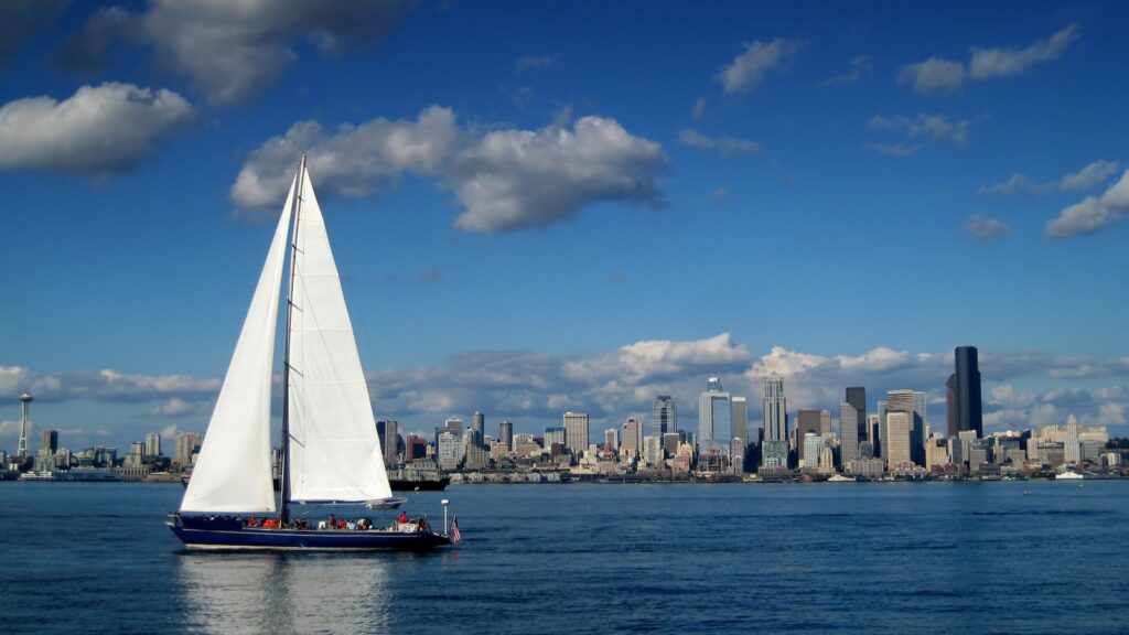 Seattle Skyline with a large sailboat in the foreground with the sails extending above the horizon. The Seattle Space Needle frames the left edge of the composition.